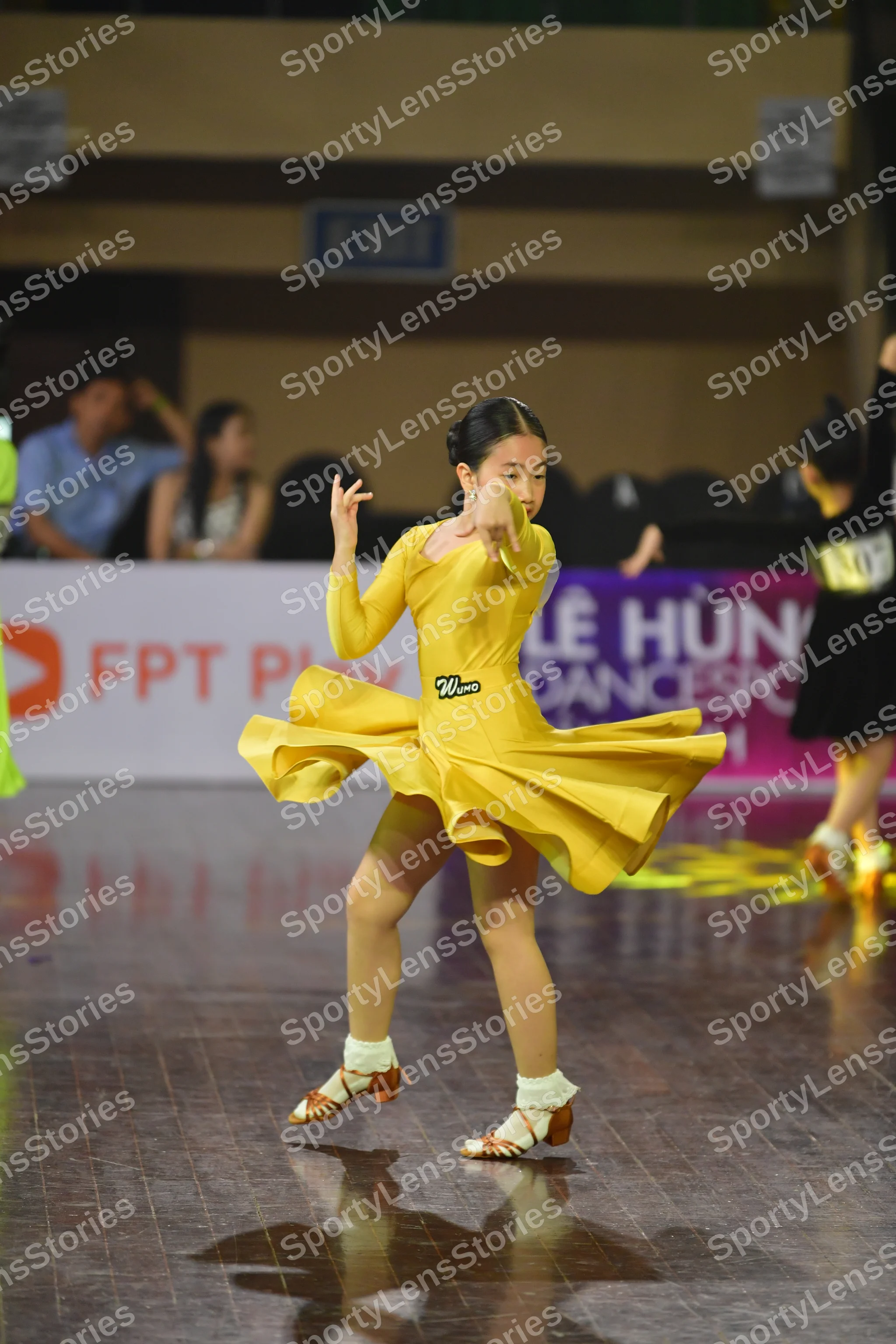 Dancesport competitor: Female dancer: yellow long-sleeved dress with a flared skirt and a small black d