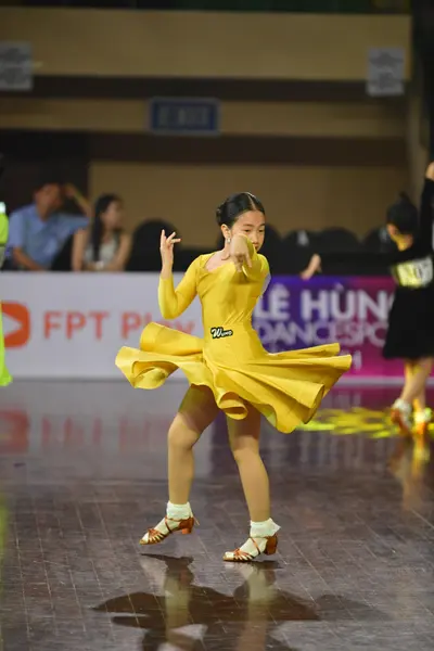 Dancesport competitor: Female dancer: yellow long-sleeved dress with a flared skirt and a small black d