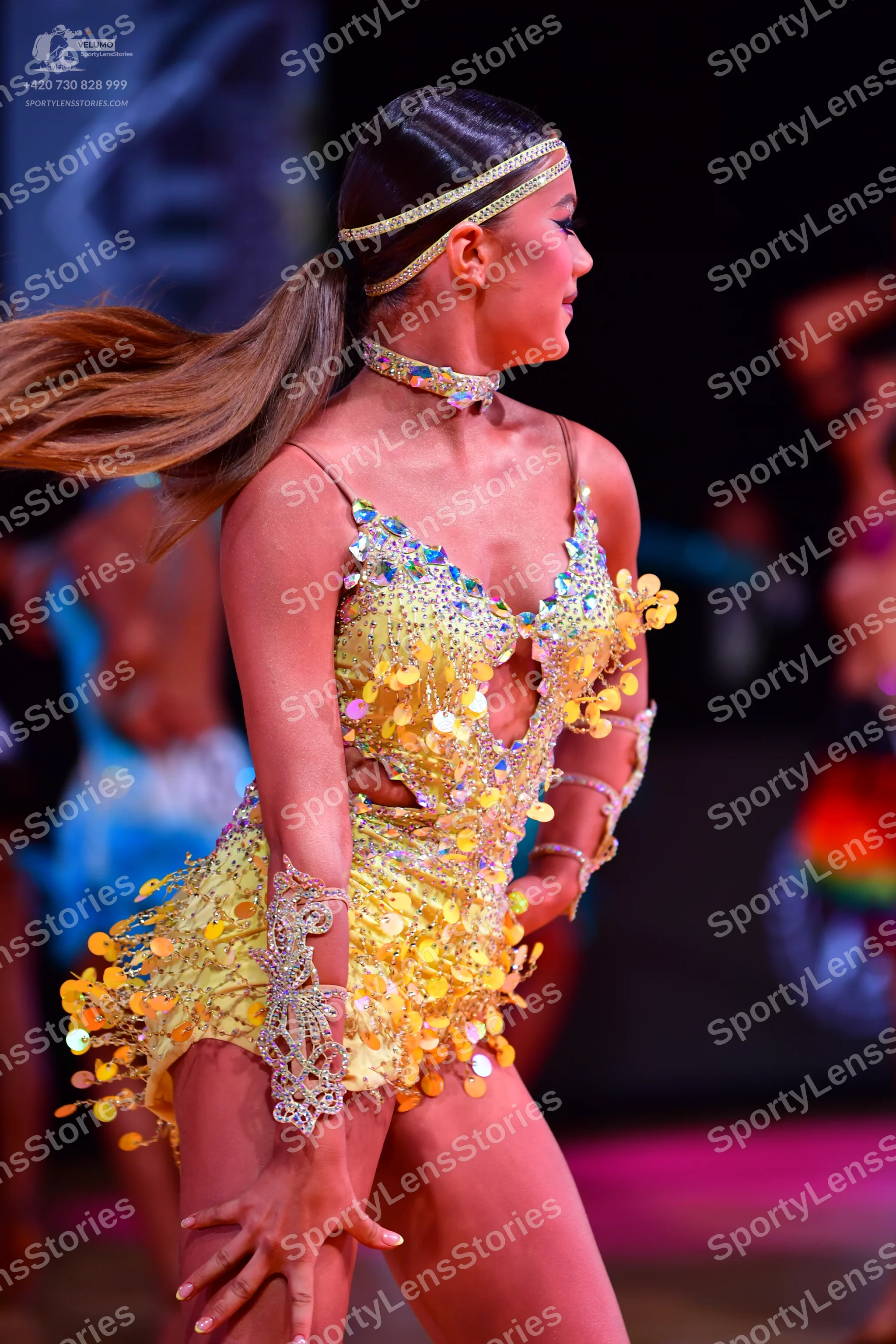 Dancesport competitor: Female dancer (foreground): yellow Latin dress embellished with large gold-color