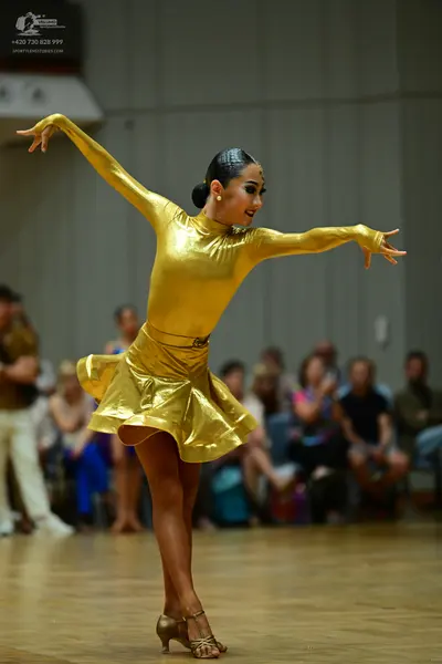 Dancesport competitor: Female dancer: gold long-sleeved Latin dress made of metallic fabric