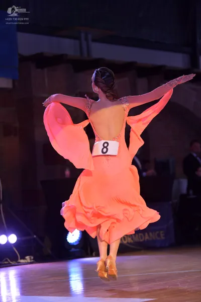 Dancesport competitor: Female dancer: orange latin dress with flowing, sheer sleeves and a low back
