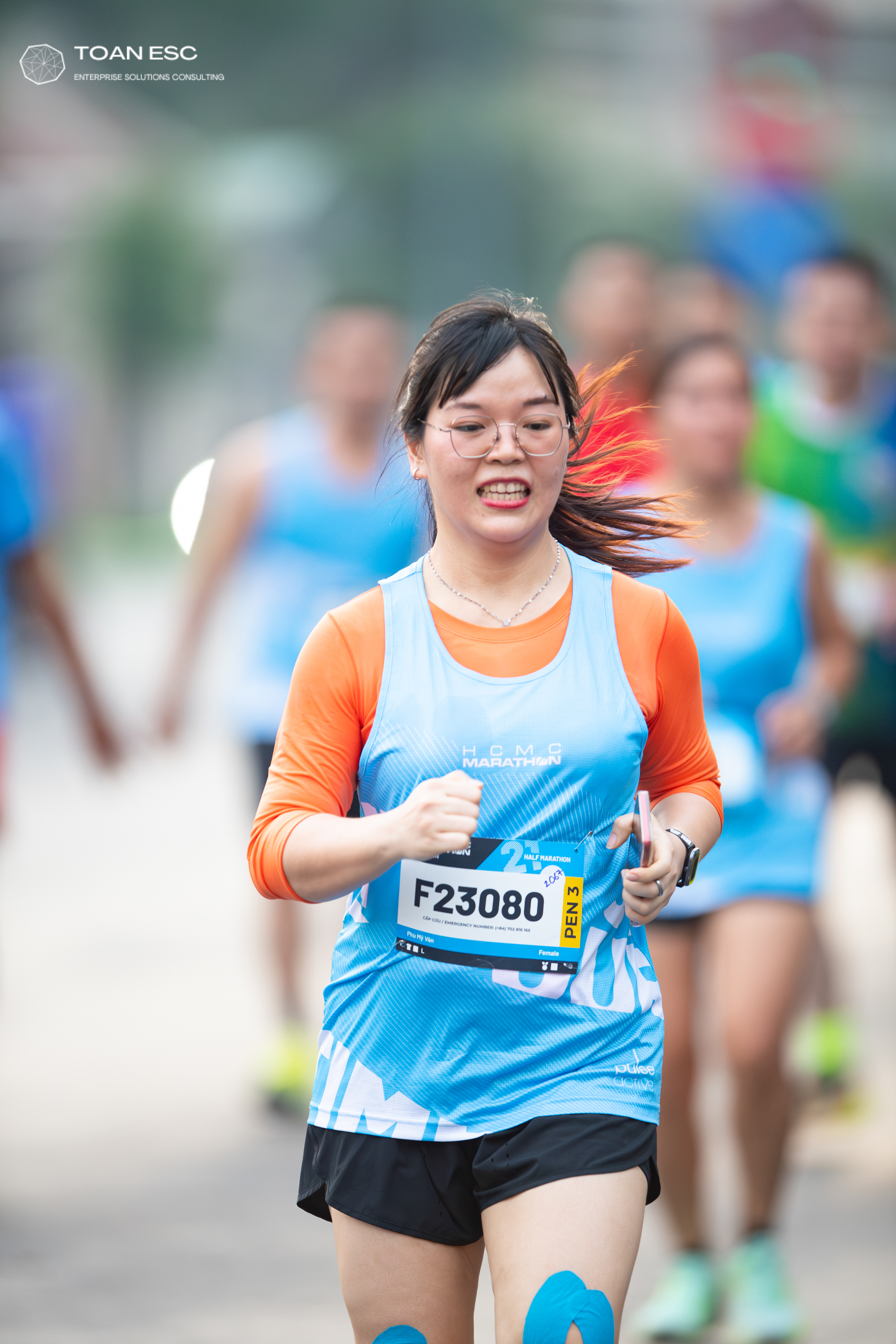 Marathon runner #F23080: Runner 1: blue patterned jersey, orange long-sleeve shirt, black shorts, glasses
