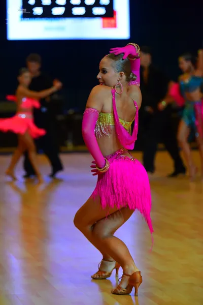Dancesport competitor: Female dancer (foreground): pink Latin costume with a gold sequined top, long pi