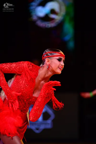 Dancesport competitor: Female dancer: red latin dress with sequins, long sleeves with fringe, and a red