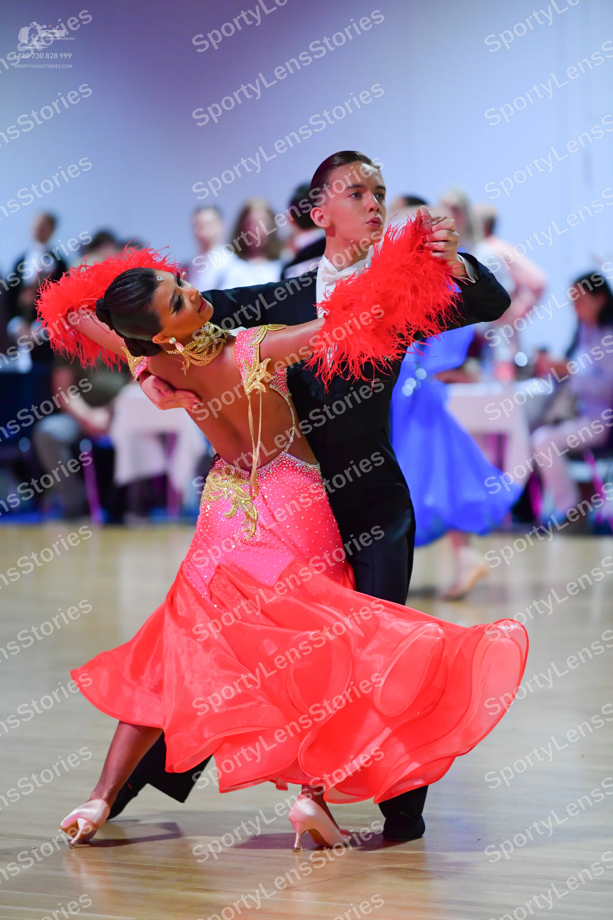 Dancesport competitor: Female dancer: pink ballroom dress with a sequined bodice, large red feather-lik