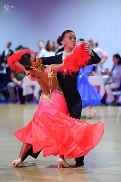 Dancesport competitor: Female dancer: pink ballroom dress with a sequined bodice, large red feather-lik