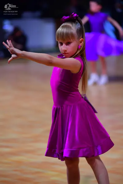 Dancesport competitor: Female dancer in foreground: magenta, satin-like, sleeveless dress with a full s
