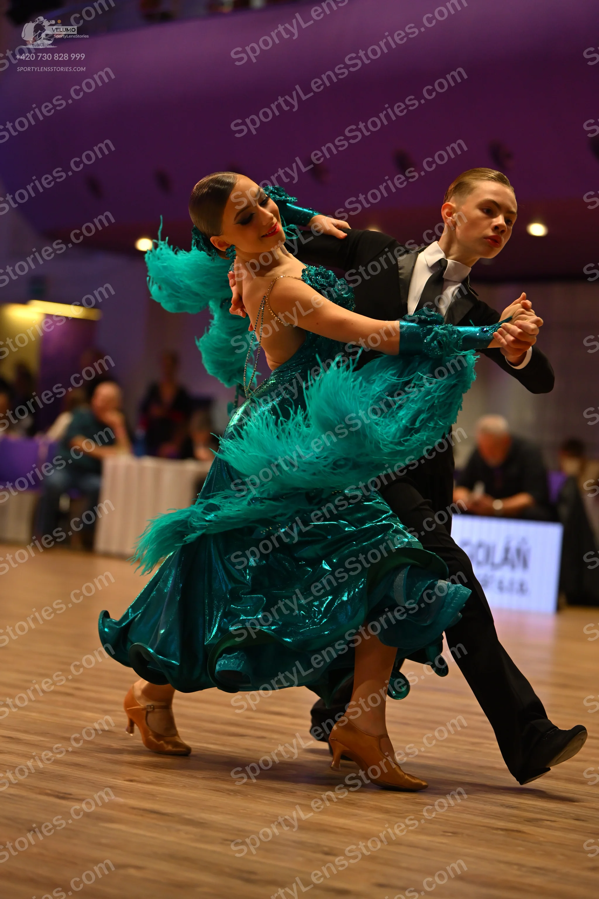 Dancesport competitor: Female dancer: teal latin dance dress with shiny, ruffled fabric and large teal 
