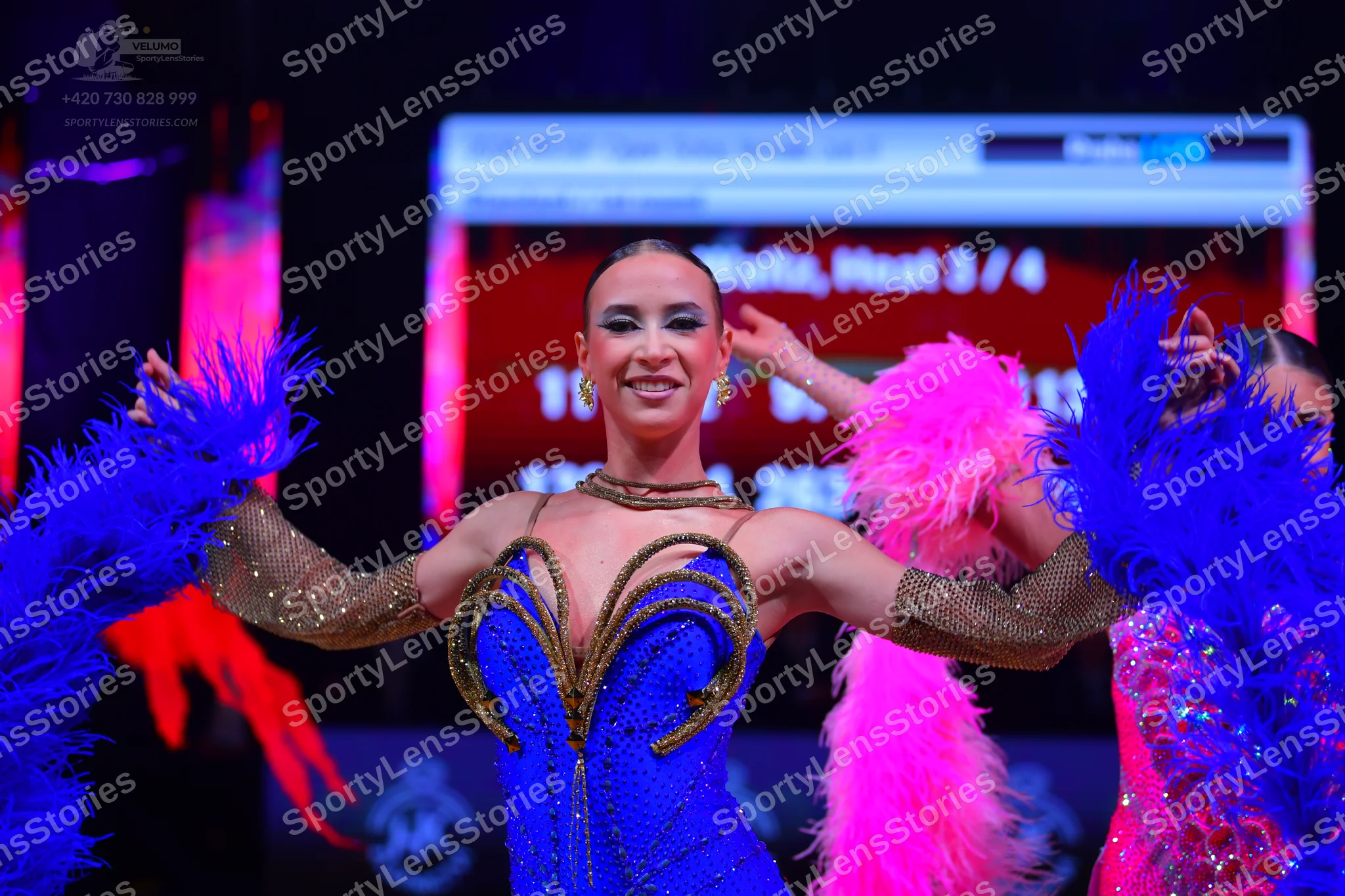 Dancesport competitor: Female dancer in center: blue sequin Latin dress with gold/bronze-colored embroi