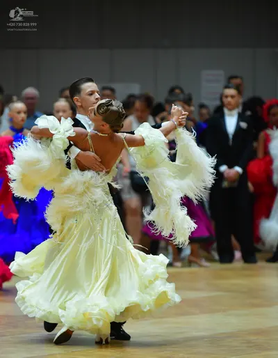 Dancesport competitor: Main female dancer: voluminous cream-colored ballroom gown with many ruffled lay