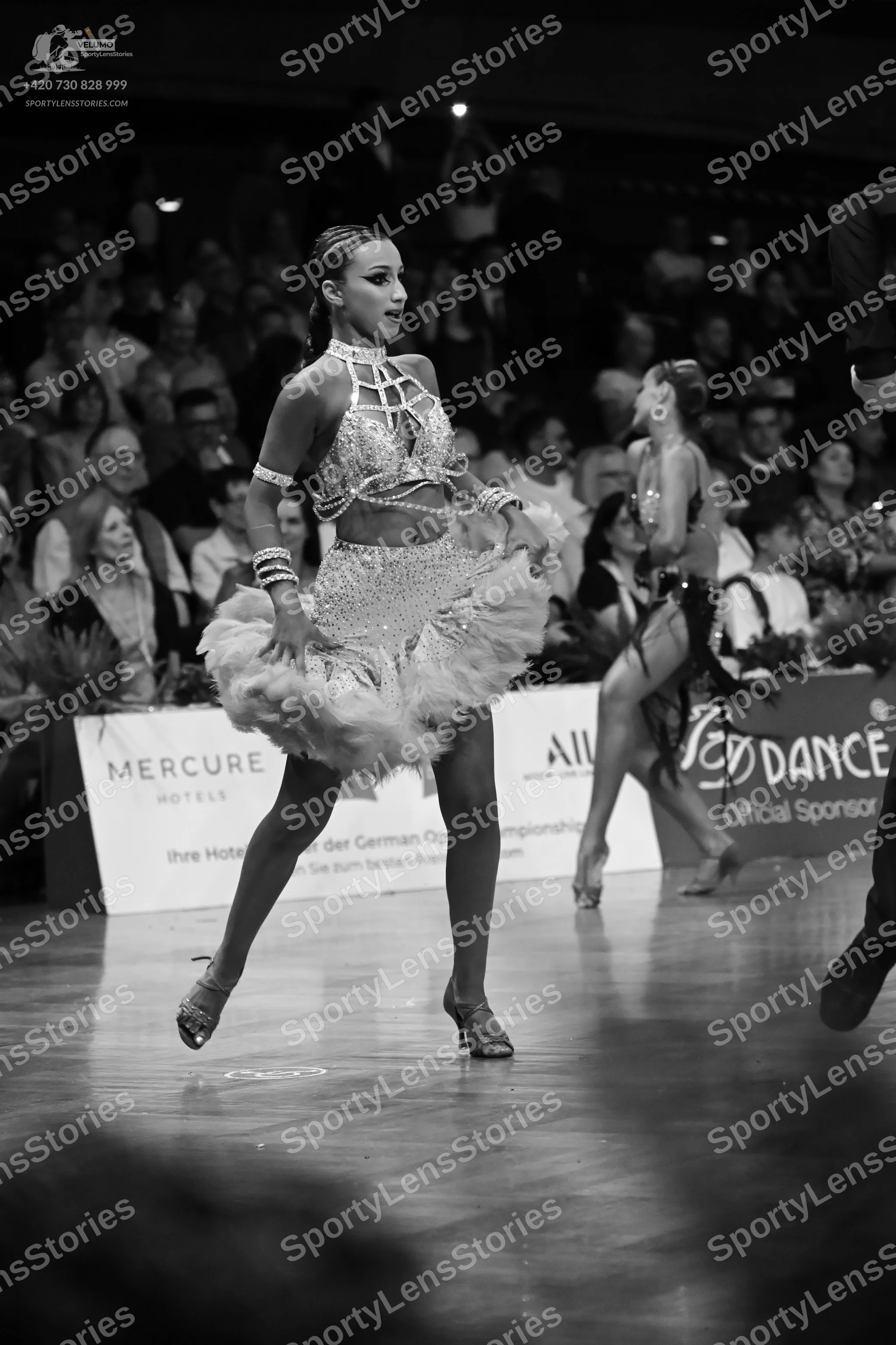 Dancesport competitor: Female dancer in foreground: light-colored Latin dance costume featuring a sequi