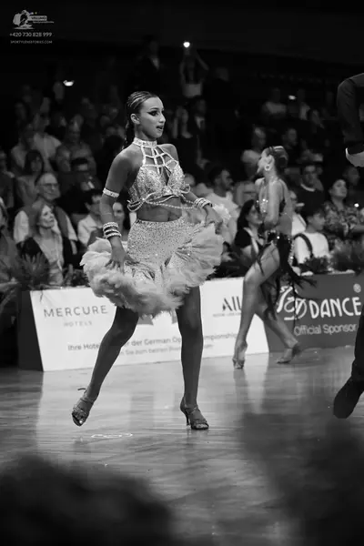 Dancesport competitor: Female dancer in foreground: light-colored Latin dance costume featuring a sequi