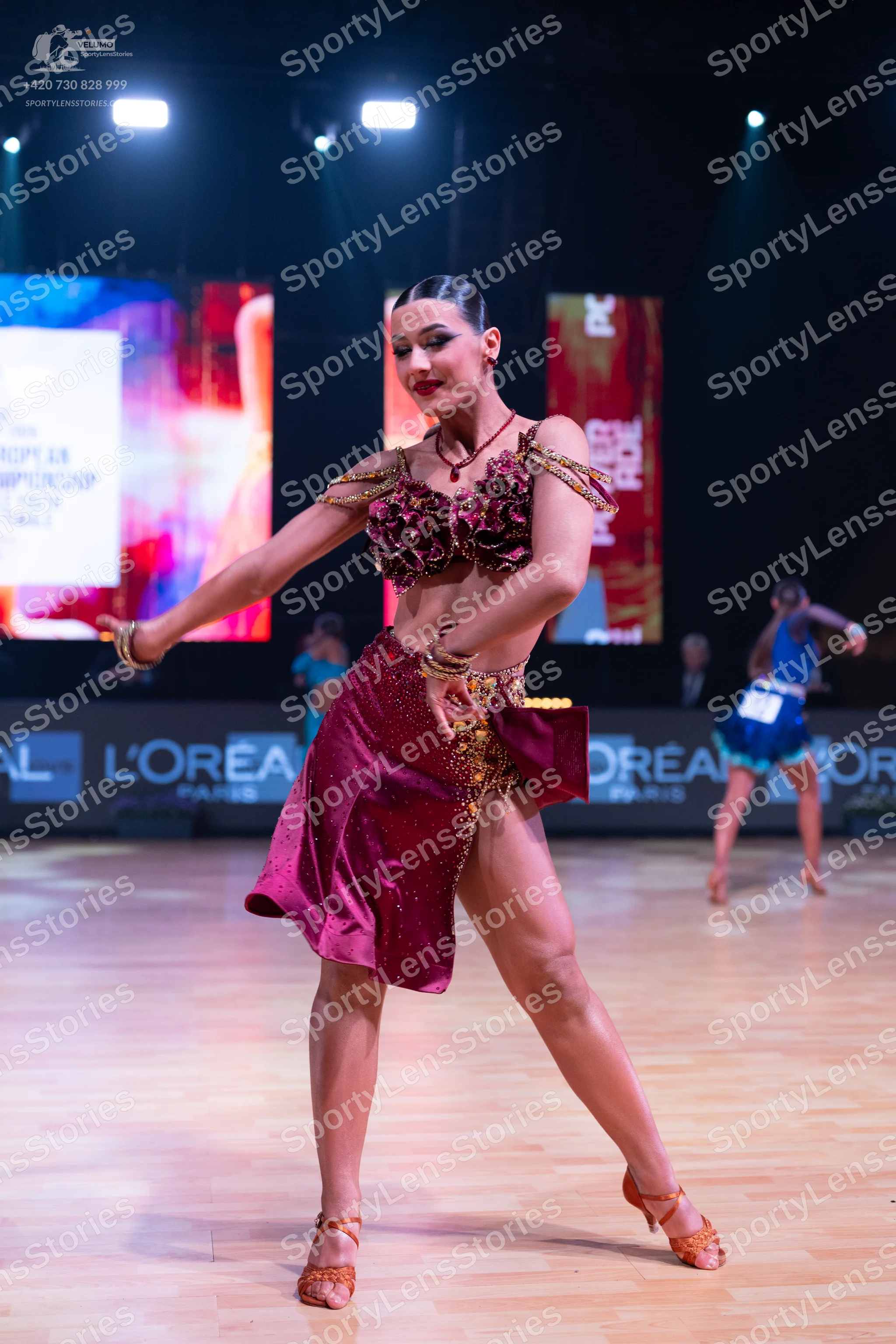 Dancesport competitor: Female dancer in foreground: burgundy Latin dance dress with gold sequin and bea