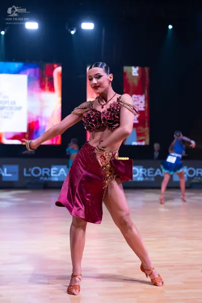 Dancesport competitor: Female dancer in foreground: burgundy Latin dance dress with gold sequin and bea