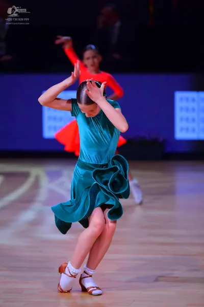 Dancesport competitor: Female dancer in foreground: teal satin Latin dress with a ruffled skirt
