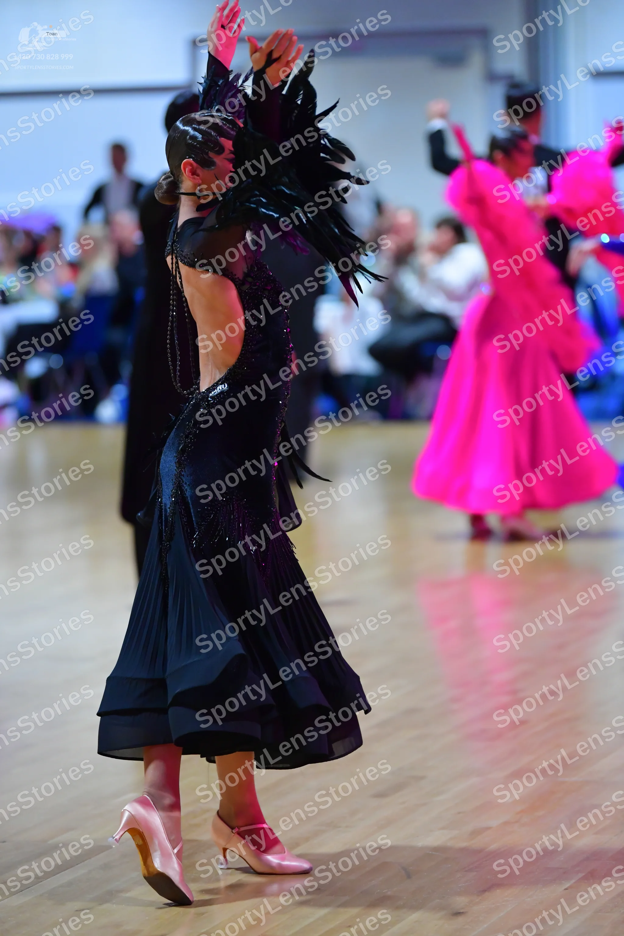 Dancesport competitor: Female dancer in foreground: black ballroom dress with a flowing skirt and drama