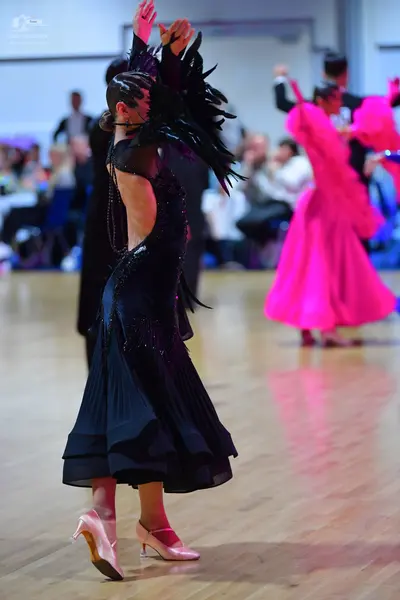 Dancesport competitor: Female dancer in foreground: black ballroom dress with a flowing skirt and drama