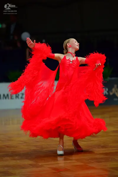 Dancesport competitor: Female dancer: red latin dress with large feather-like fringe on sleeves and ski