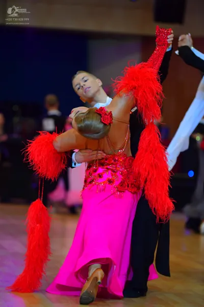 Dancesport competitor: Female dancer: pink ballroom gown with red sequin embellishments and large red f