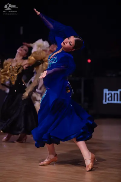 Dancesport competitor: Female dancer in foreground: royal blue ballroom gown with sheer blue sleeves an