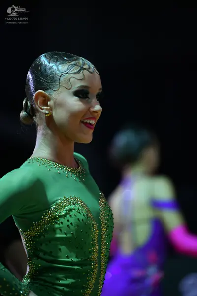 Dancesport competitor: Female dancer in foreground: green long-sleeved Latin dress with gold rhinestone