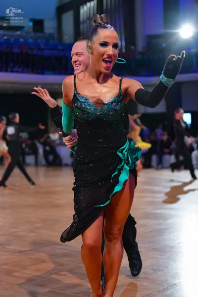 Dancesport competitor: Female dancer: black latin dress with sequined bodice, teal/green ruffles, and l