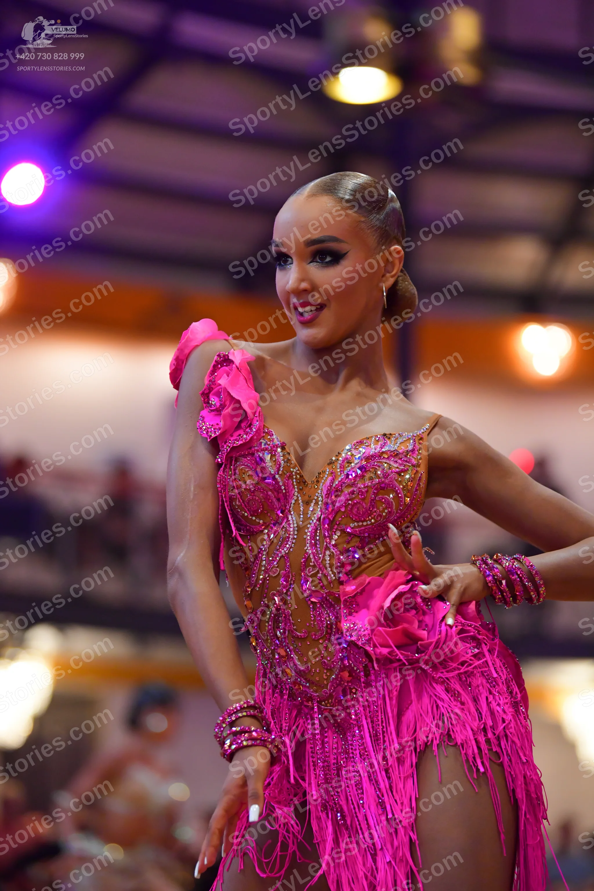 Dancesport competitor: Female dancer: bright pink latin dress with fringe, sequins, and large fabric fl