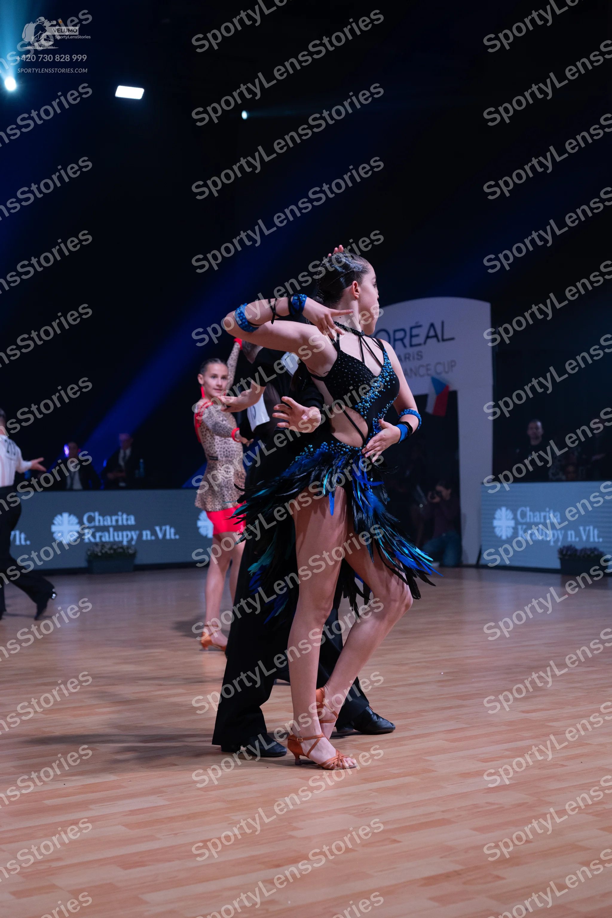 Dancesport competitor: Female dancer (foreground): black latin dress with a strappy/netted bodice, long