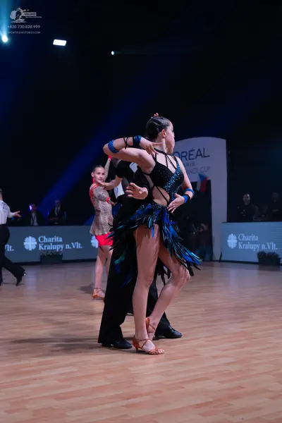 Dancesport competitor: Female dancer (foreground): black latin dress with a strappy/netted bodice, long