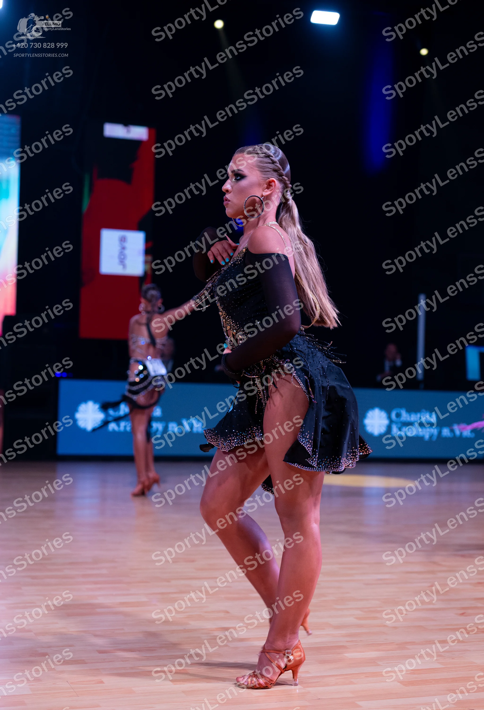 Dancesport competitor: Female dancer in foreground: black latin dress with sequins and long sheer black