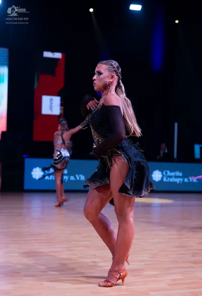 Dancesport competitor: Female dancer in foreground: black latin dress with sequins and long sheer black