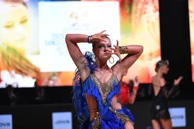Dancesport competitor: Female dancer in foreground: blue latin dress with gold sequins and fringe, acce