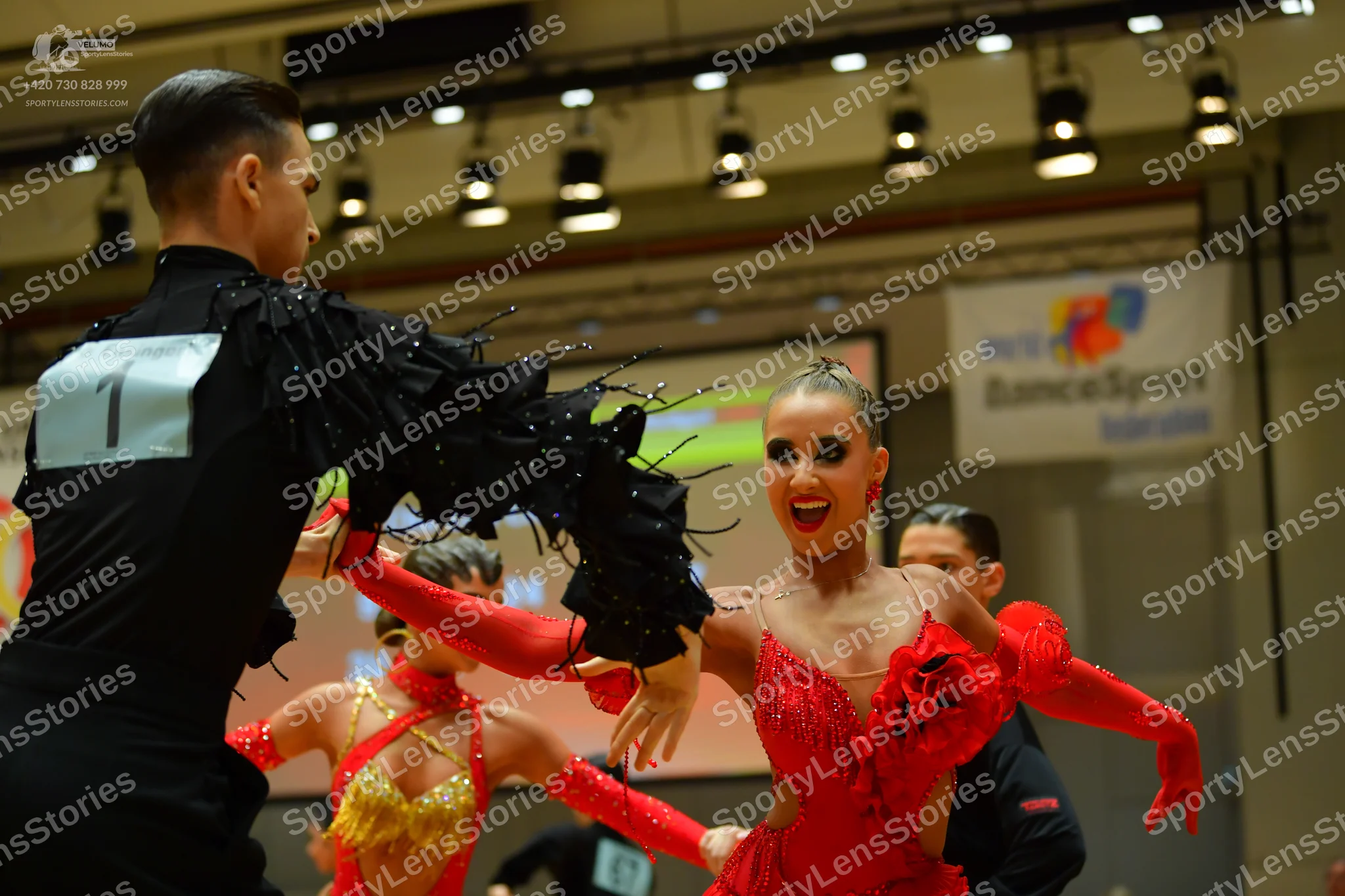 Dancesport competitor: Male dancer (foreground): black long-sleeved shirt with black fringe detailing o