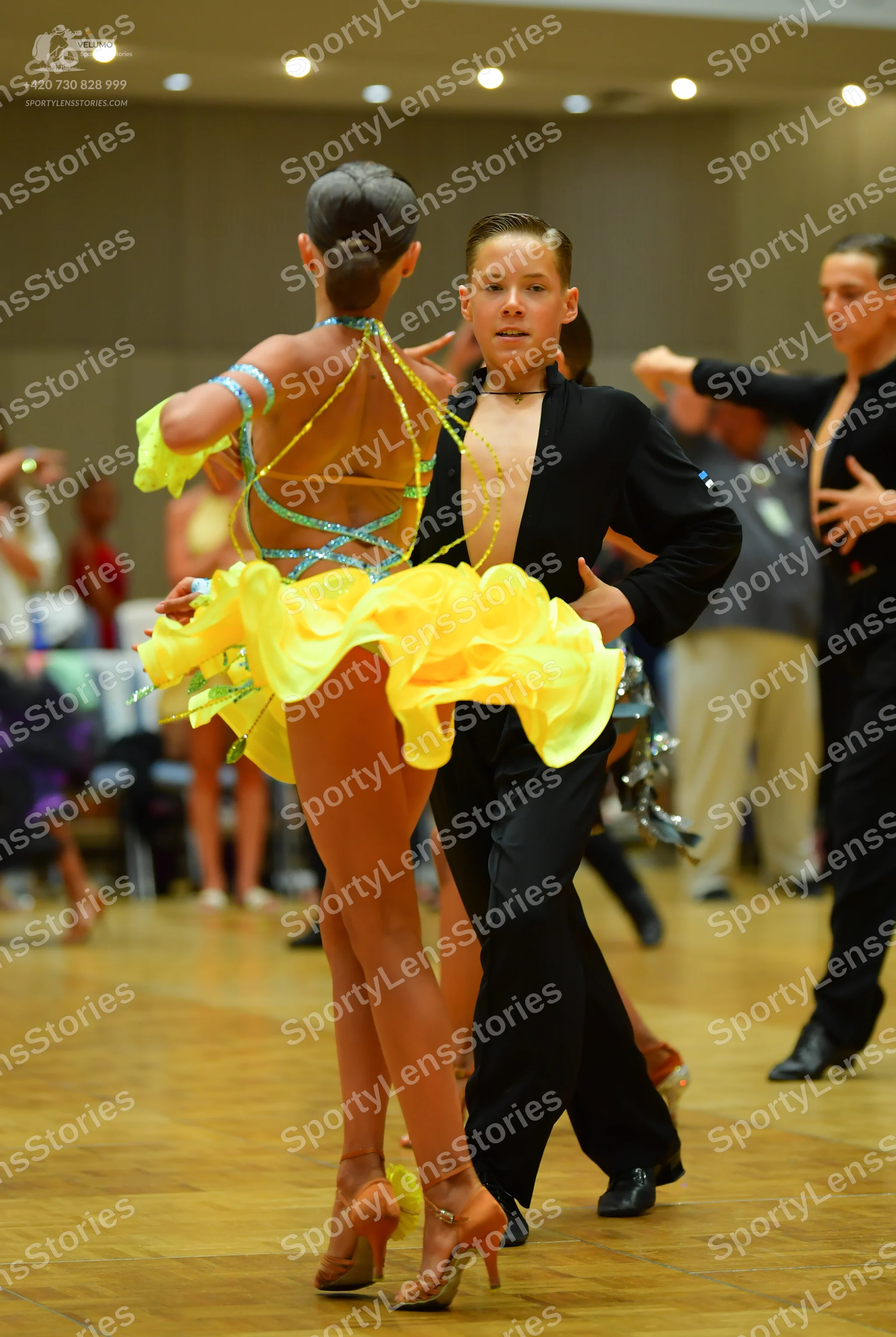 Dancesport competitor: Female dancer: yellow Latin dance costume with thin, sparkly blue/teal straps ac