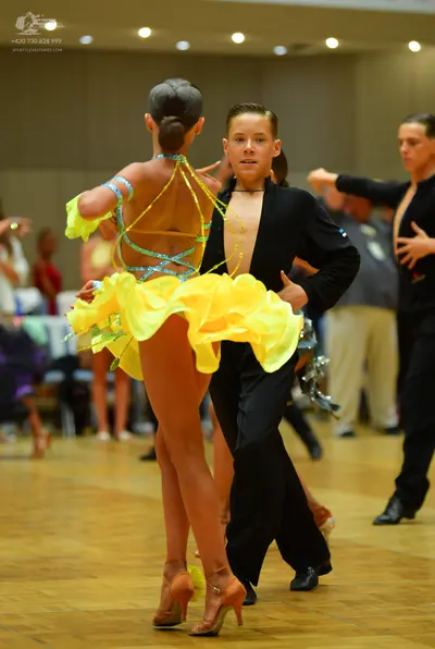 Dancesport competitor: Female dancer: yellow Latin dance costume with thin, sparkly blue/teal straps ac