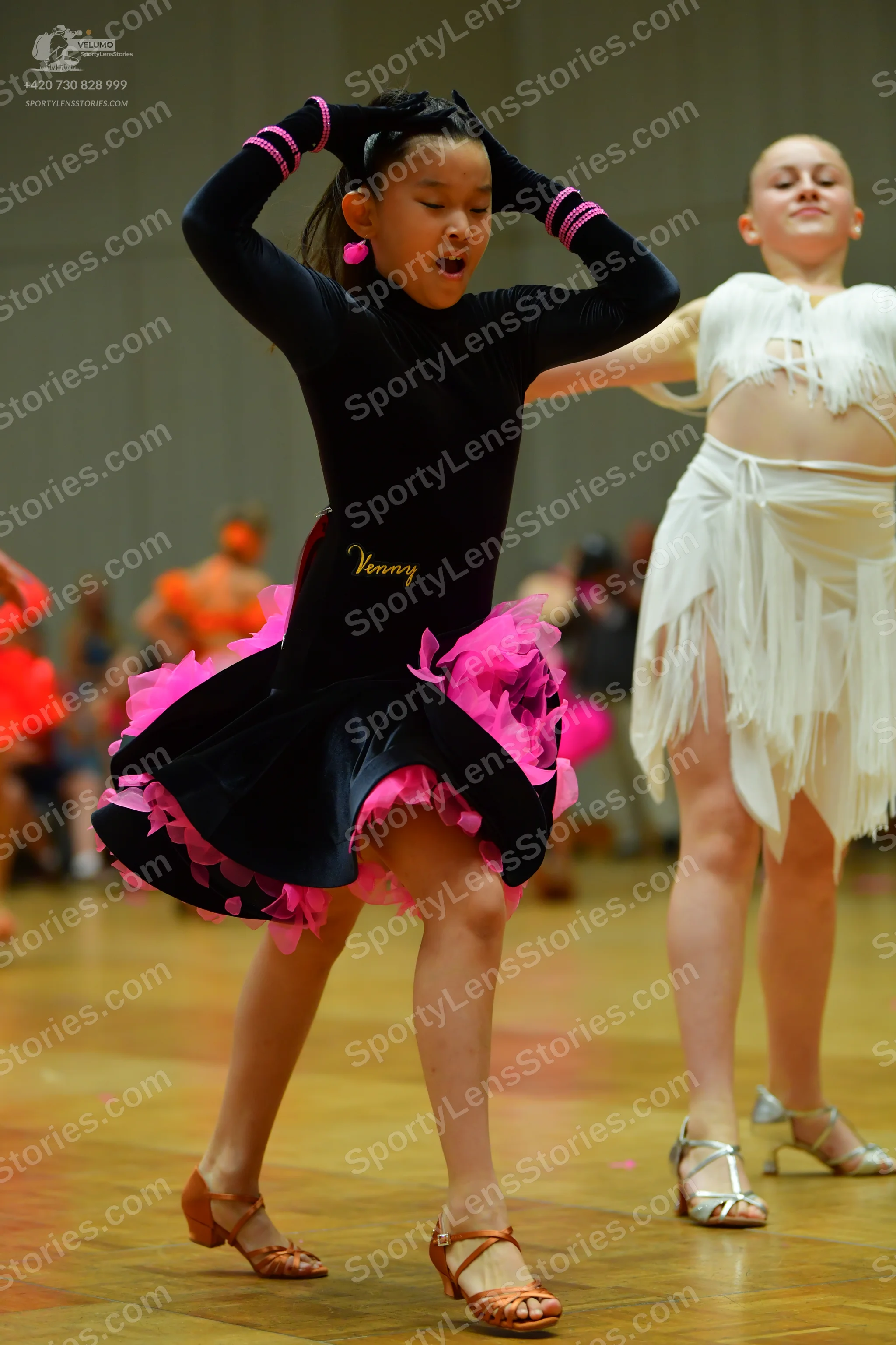 Dancesport competitor: Female dancer in foreground: black long-sleeved Latin dance dress with pink stri