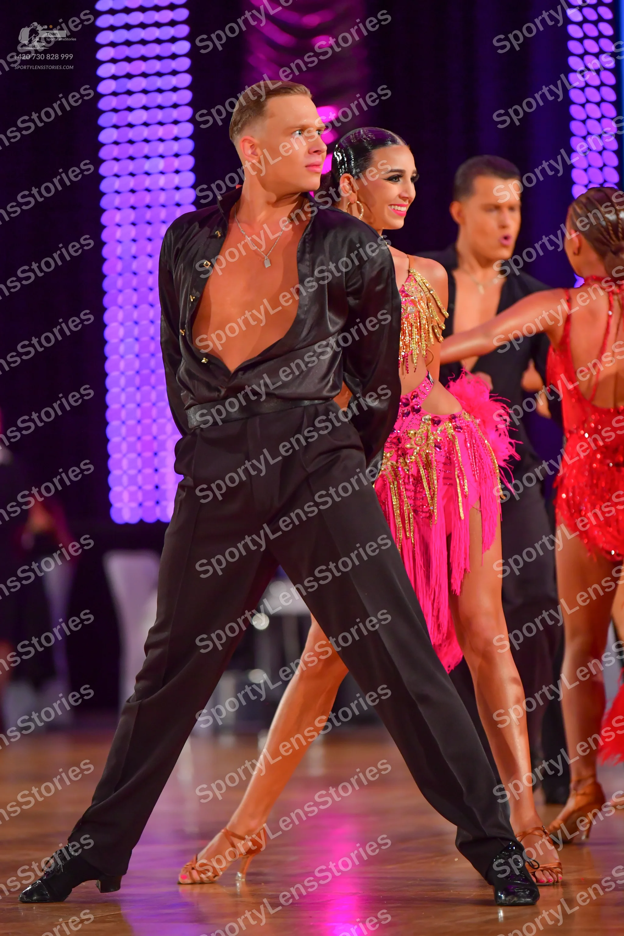 Dancesport competitor: Male dancer (foreground): black satin shirt, open at the chest, black trousers,