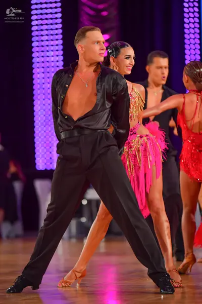 Dancesport competitor: Male dancer (foreground): black satin shirt, open at the chest, black trousers, 