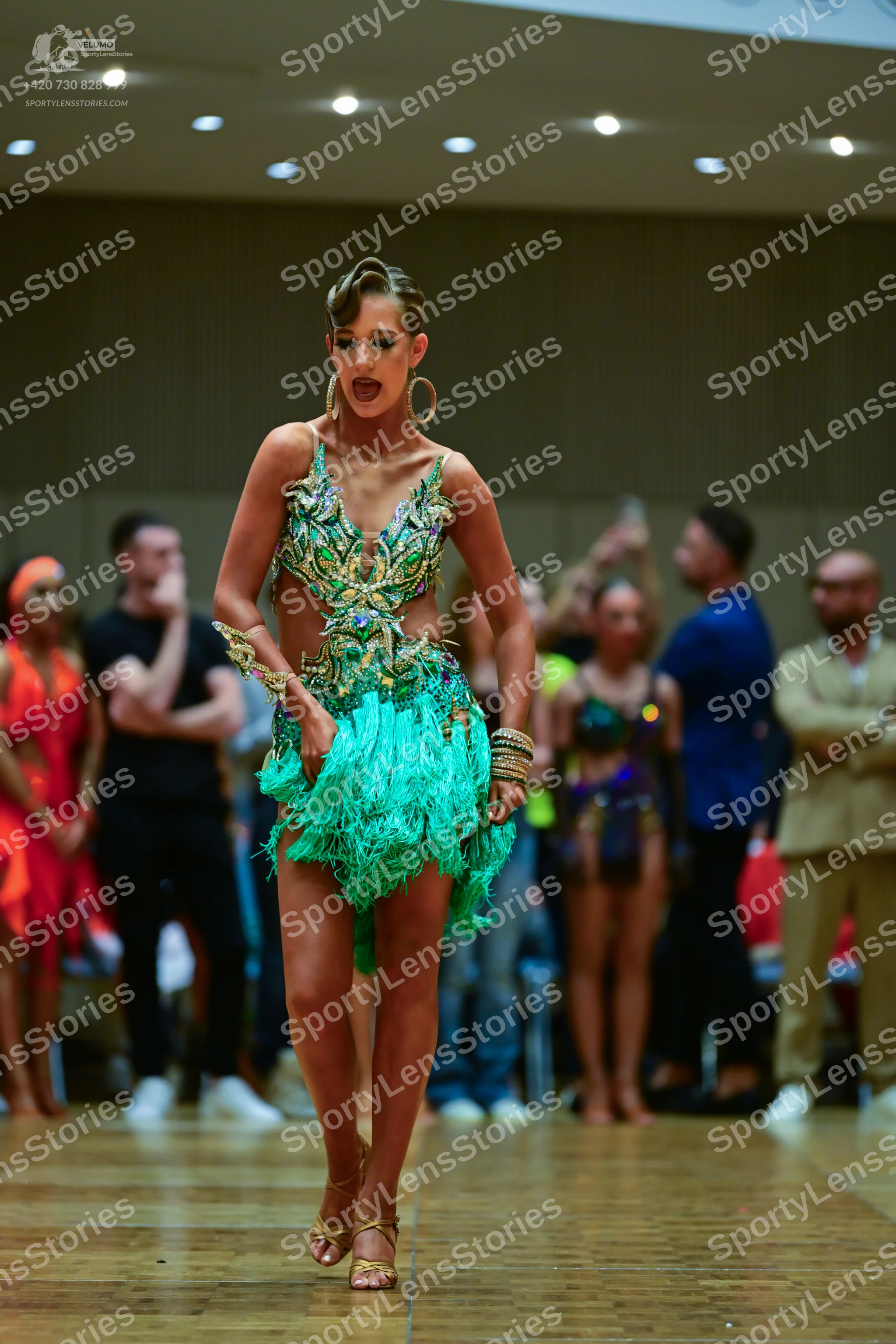 Dancesport competitor: Main female dancer: green and gold sequined Latin dress with a fringe skirt, acc