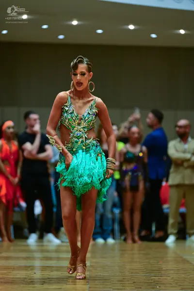 Dancesport competitor: Main female dancer: green and gold sequined Latin dress with a fringe skirt, acc
