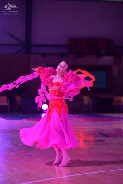 Dancesport competitor: Female dancer: bright pink ballgown with voluminous, ruffled layers of fabric