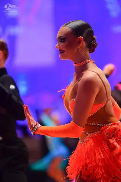 Dancesport competitor: Female dancer: orange latin dress with sequins, fringe, thin straps, and long sl