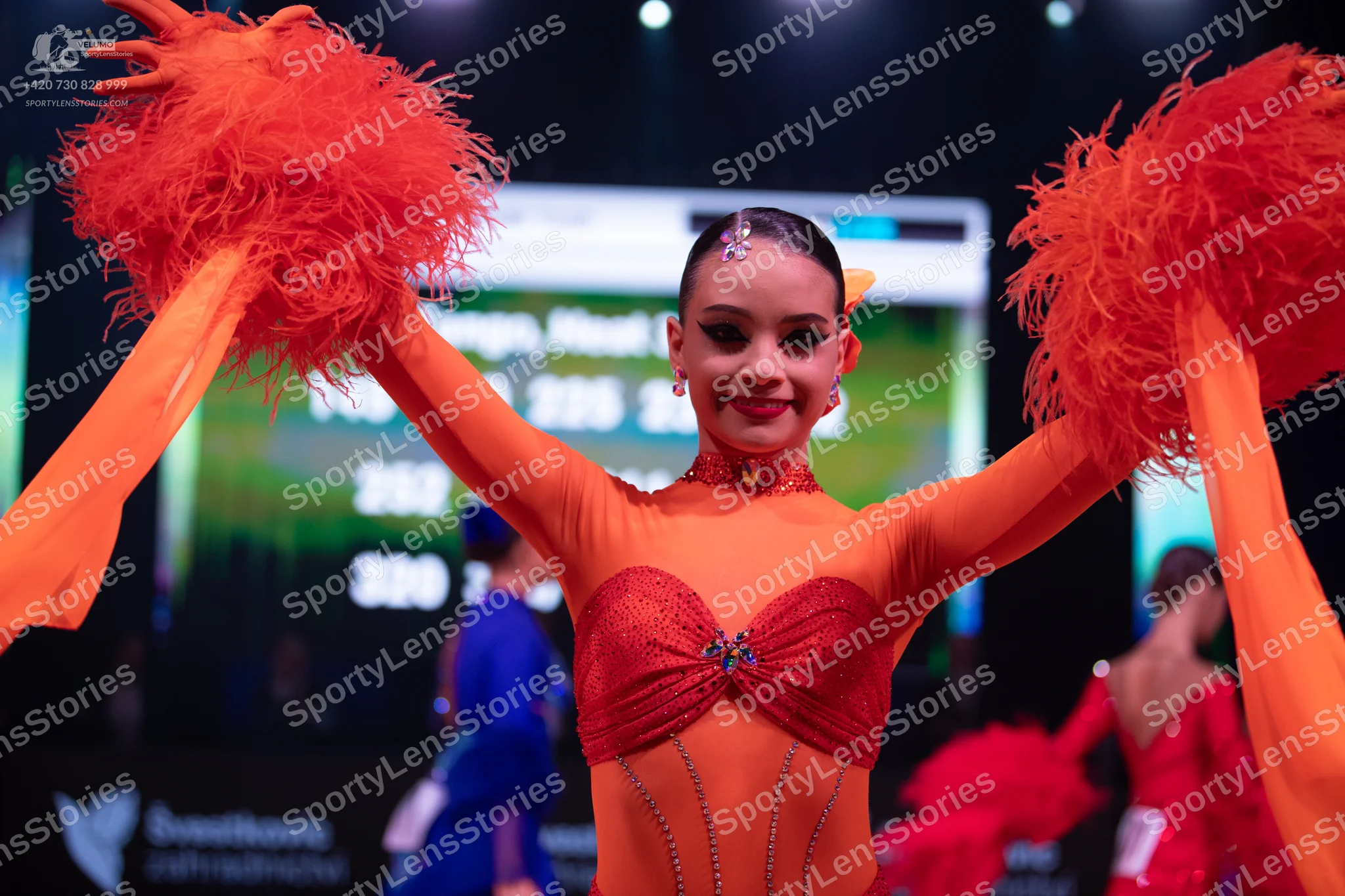 Dancesport competitor: Female dancer in foreground: orange and red Latin dance costume with a sheer ora