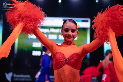 Dancesport competitor: Female dancer in foreground: orange and red Latin dance costume with a sheer ora
