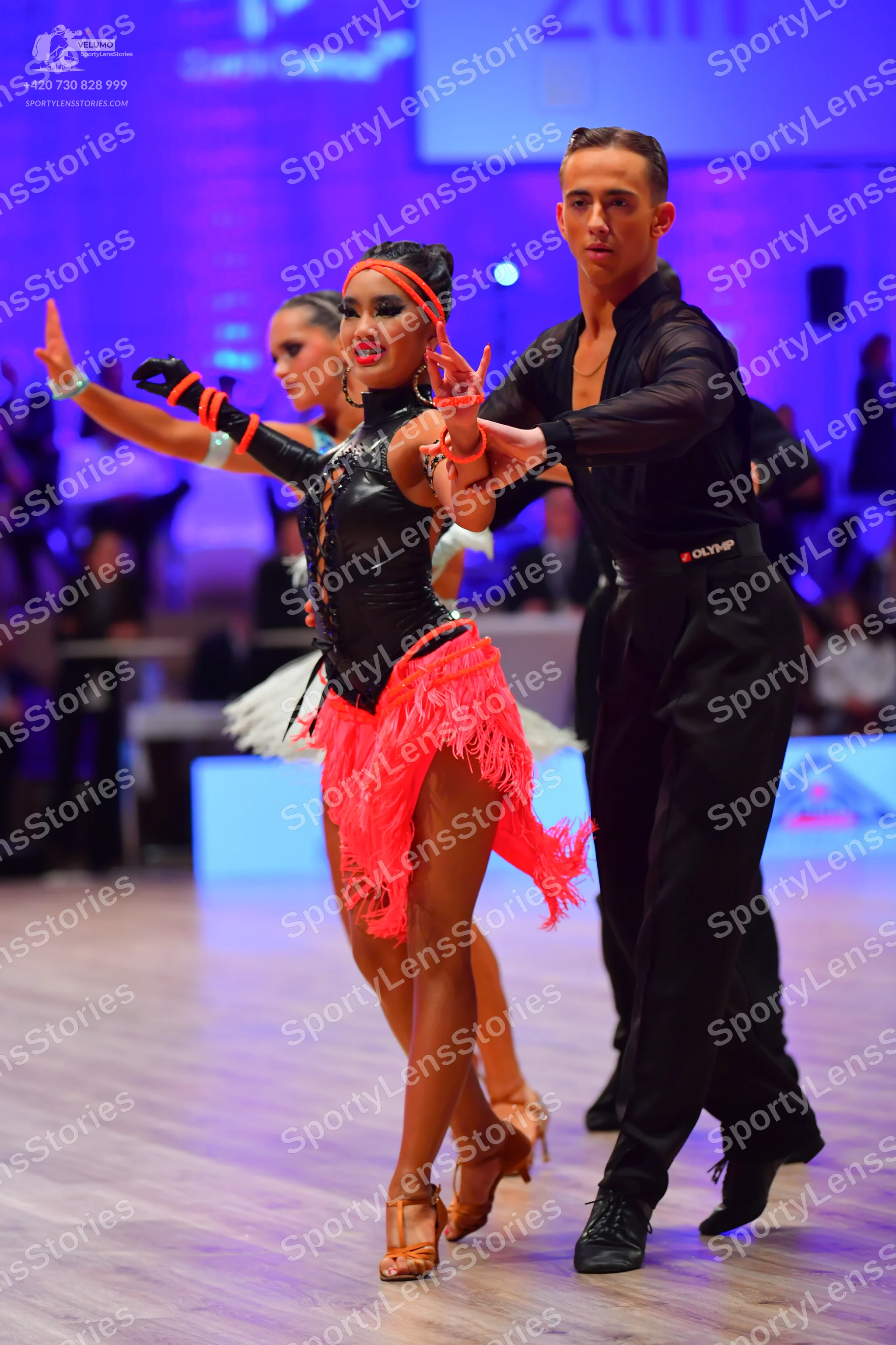 Dancesport competitor: Female dancer: black long-sleeved top with lace-up side detailing and a bright p