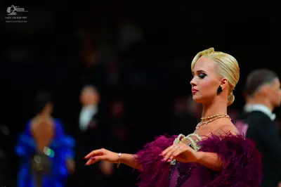 Dancesport competitor: Female dancer in foreground: dark purple latin dress with large feather trim on 