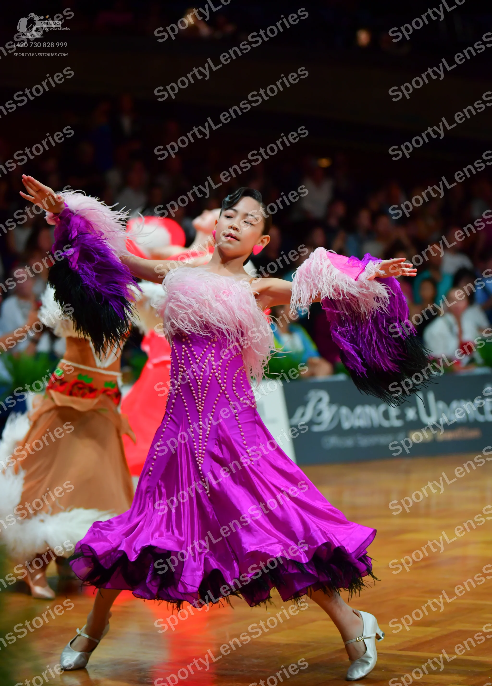 Dancesport competitor: Foreground dancer: fuchsia satin ballroom dress with pink and dark purple feathe