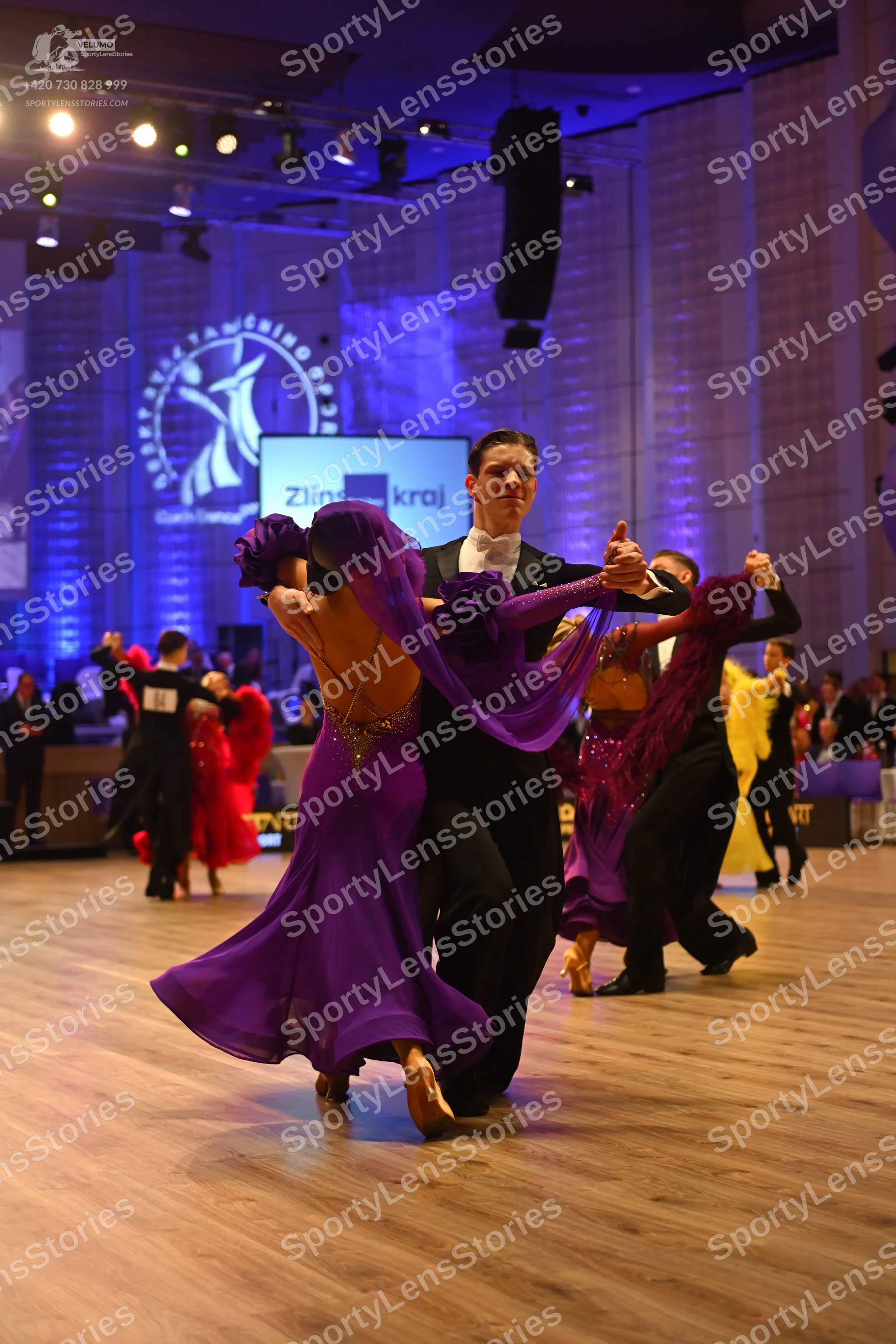Dancesport competitor: Female dancer in foreground: purple latin dress with sequins and a flowy skirt