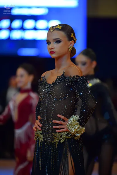 Dancesport competitor: Female dancer in foreground: black long-sleeved latin dress with sequins, gold l