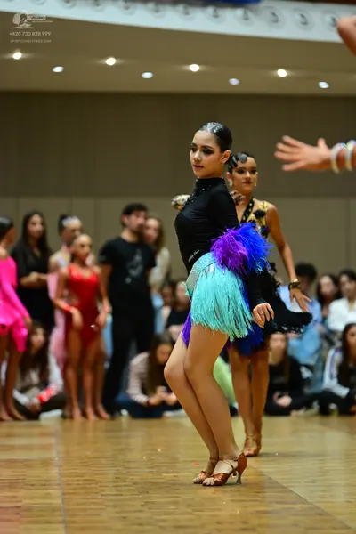 Dancesport competitor: Main female dancer: black long-sleeved top with a multi-colored fringe skirt in 